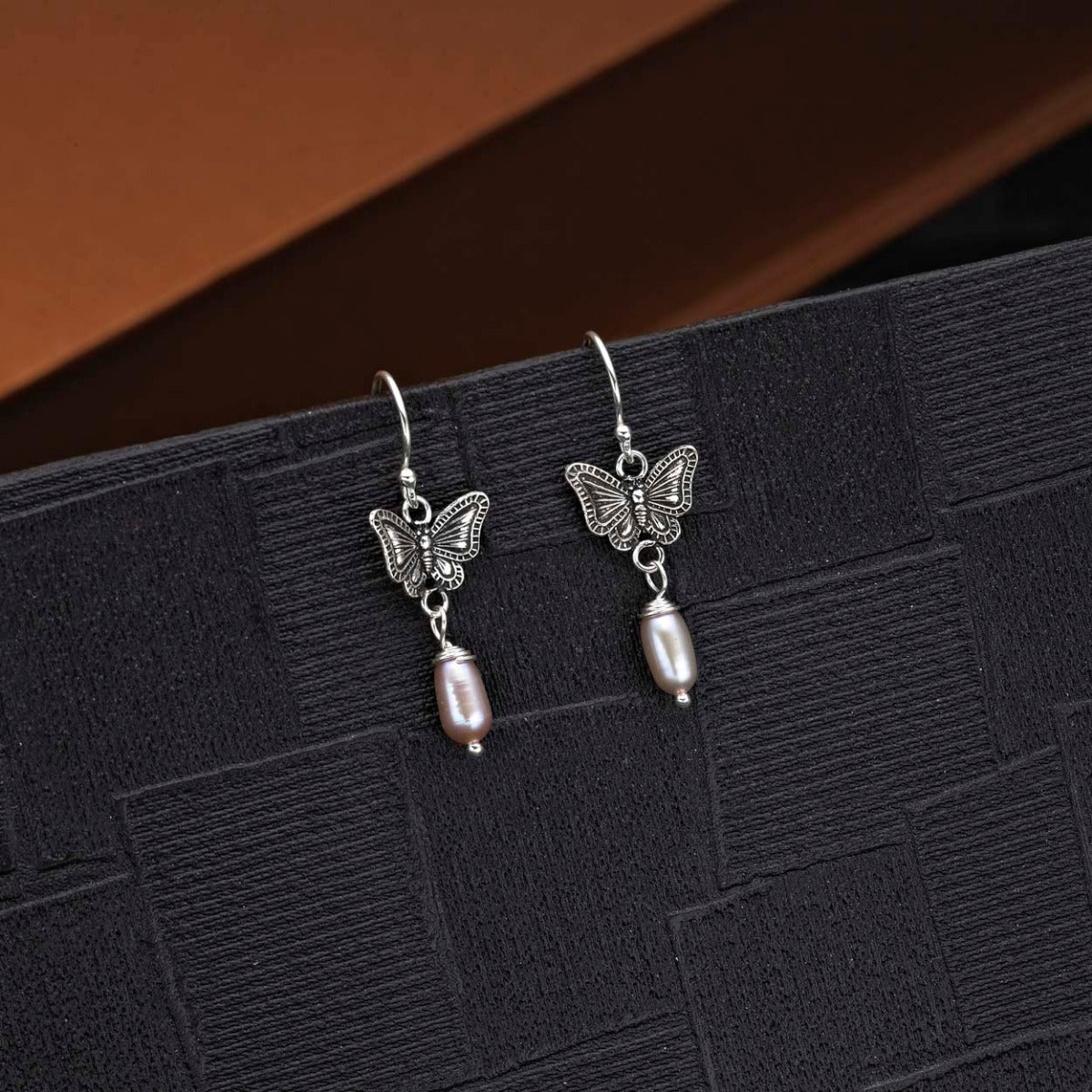 Pearl and Oxidised Butterfly Drop Earrings in 925 Sterling Silver on black surface